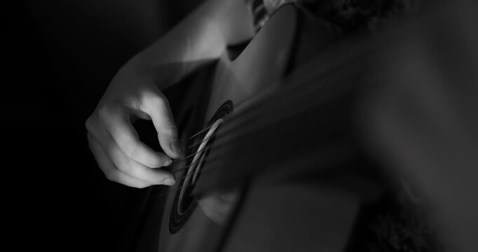 Cinematic black and white close-up of a musician's hand delicately plucking the strings of a classical guitar near the sound hole, captured with dramatic high-contrast lighting.
