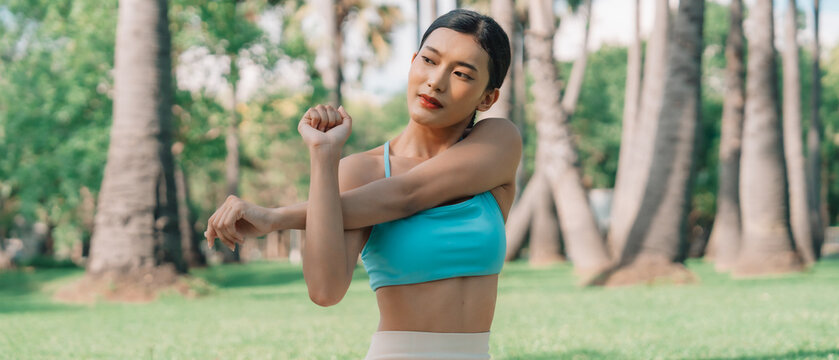 Asian woman practicing seated side stretch yoga pose outdoors in a peaceful park, wearing athletic wear. Promotes mindfulness, flexibility, and a healthy, balanced lifestyle surrounded by nature