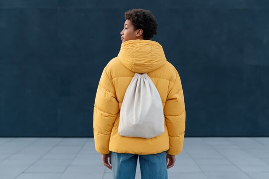Rear view of person in yellow puffer jacket with white drawstring backpack for lifestyle fashion advertisement background and product mockup