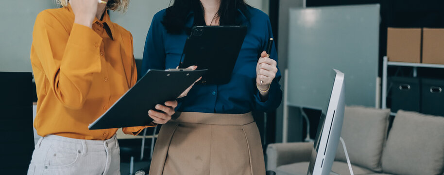 Two businesswomen discussing work using a laptop in a modern office lounge area, showing teamwork and communication
