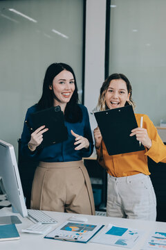 Two businesswomen discussing work using a laptop in a modern office lounge area, showing teamwork and communication