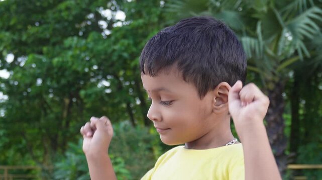 Happy young boy raising fists outdoors in park with joyful expression