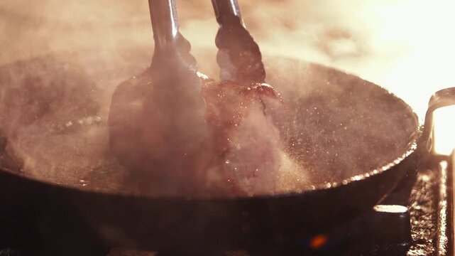 Chef cooks pork chop on a hot griddle with tongs in a restaurant