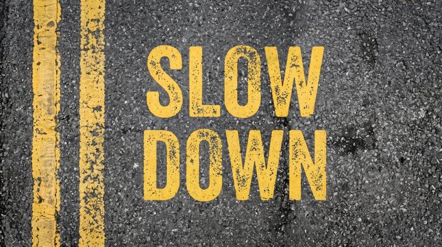 Slow down warning painted in yellow stencil letters on cracked asphalt beside double road lines