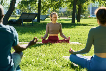 Caucasian young adult woman instructor leading outdoor yoga meditation session with diverse group...