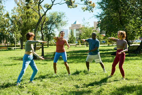 Diverse multiethnic group including African American man practicing tai chi or qigong gymnastics in park. Useful for fitness marketing and wellness campaigns