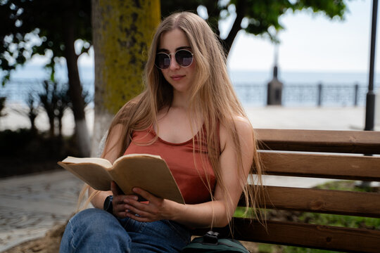 Female reader enjoying a quiet afternoon with a book on a waterfront promenade. Casual outdoor leisure and mindful lifestyle concept.