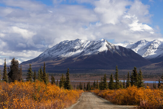 Scenic dirt road leading to snow capped mountains in fall