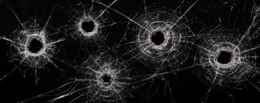 Multiple bullet holes have shattered a glass surface, creating spiderweb-like cracks radiating from each impact point.