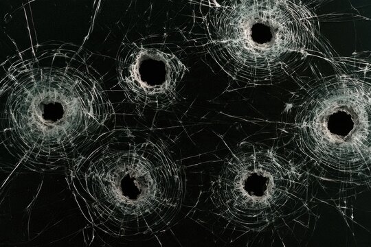 Six bullet holes in a shattered glass surface, showing radiating cracks on a dark background.
