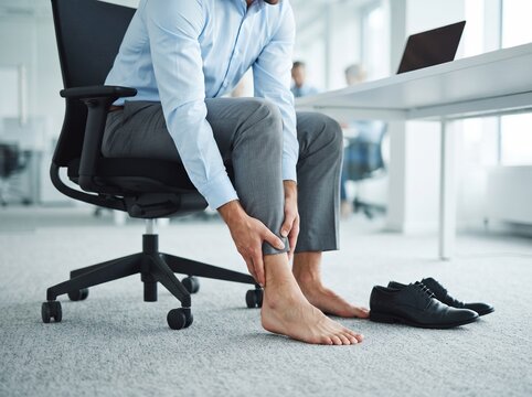 Business professional in office sitting in ergonomic chair holding his bare foot in pain with discomfort soreness professional strained ergonomic businessman physical wellness suffering