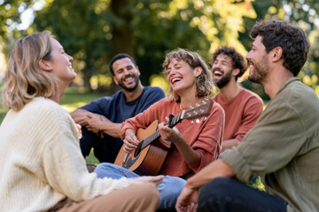 Obraz premium Diverse friends sing and play guitar together outdoors. Live music, joyful gathering, social connection.