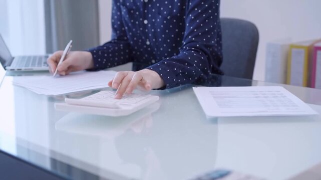Female accountant is using a laptop computer and calculator for counting taxes at a glass desk in office. Woman in business audit and finance