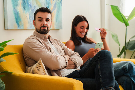 A warm couple sits on a bright yellow sofa, sharing a smartphone moment. The scene conveys casual, comfortable focus and everyday connection during a quiet indoor afternoon.