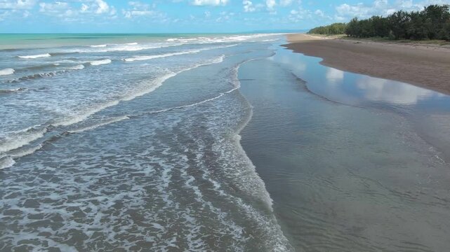 Beautiful tropical coastline viewed from above, featuring turquoise ocean water, rolling waves, wet sand and lush coastal vegetation. Peaceful natural scenery suitable for travel and vacation concepts