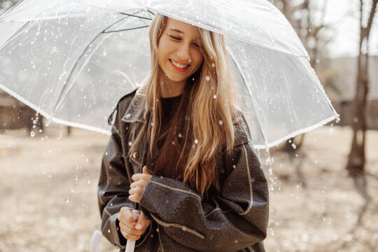 Smiling girl with transparent umbrella in rainy park