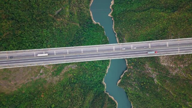 Aerial clockwise orbit shot overlooking highway suspension bridge traffic spanning a river valley on an overcast day.