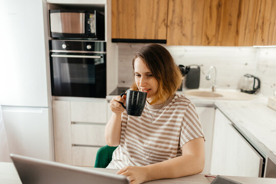 Woman drinking coffee while working remotely on laptop