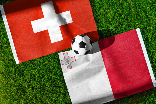 Switzerland vs. Malta football match. National flags on green grass with soccer ball in the middle. Football background for international match.