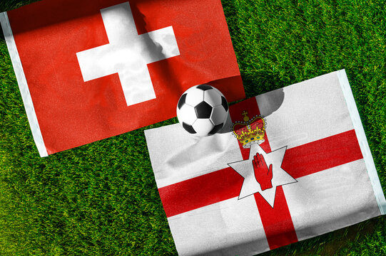 Switzerland vs. Northern Ireland football match. National flags on green grass with soccer ball in the middle. Football background for international match.