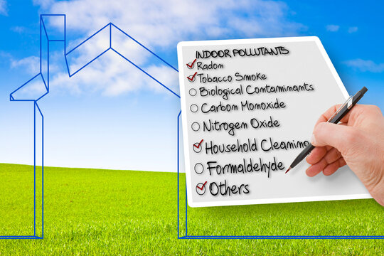 Hand writing a check list of indoor air pollutants against an outline of a little home with a grass area on background - concept image with copy space