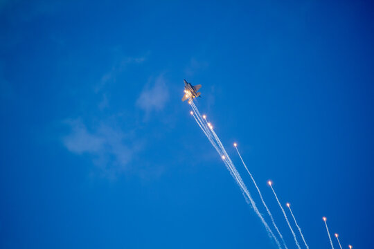 F-35A Lightning II fighter aircraft flying across a blue sky with visible vapor trails and clouds below, photographed in side profile showing its distinctive stealth aircraft design.