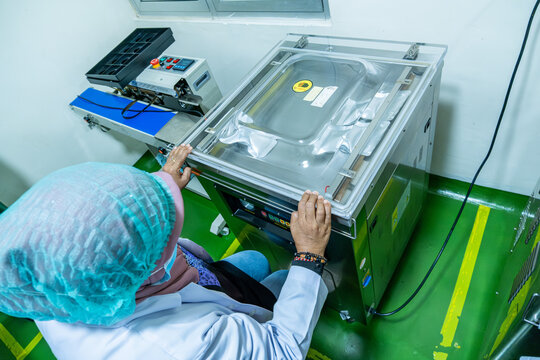 Worker in protective clothing operates a commercial food packaging machine in a hygienic processing facility for safe and efficient product handling.