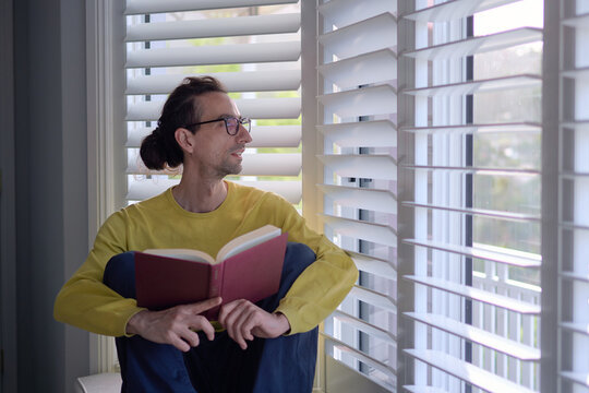 Smiling Man Reading Book Near Window Looking Sideways