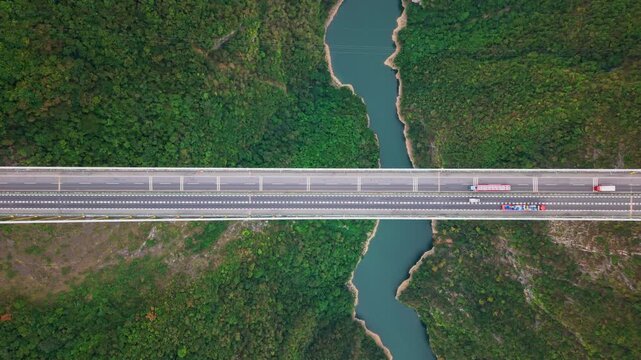 Aerial hover shot overlooking vehicle traffic on a highway suspension bridge crossing a scenic river valley on an overcast day.