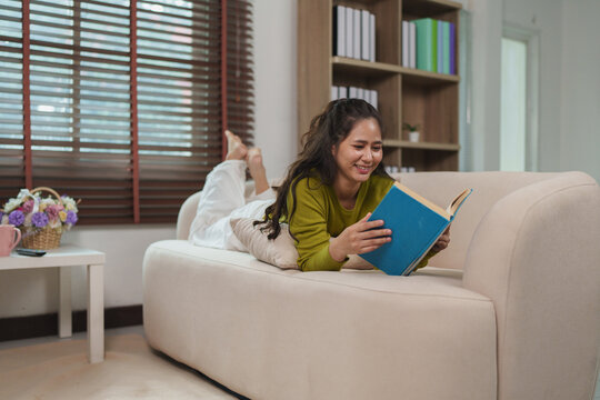 Woman smiling reading book relaxing on sofa at home