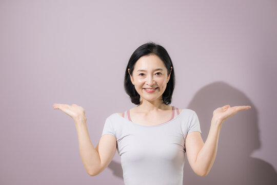 両手を広げて二つの選択肢を比較する日本人ミドル女性、スポーツ系の商品やサービスの違いを紹介する笑顔の女性