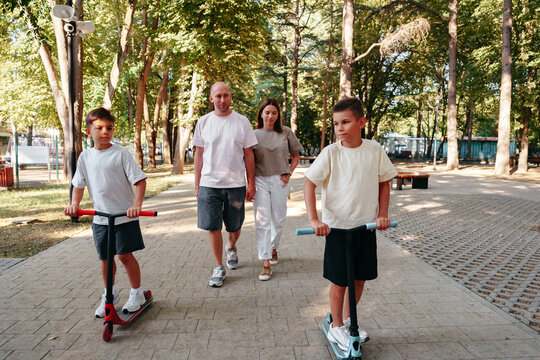 Family walks in the park with kids riding scooters during a sunny day