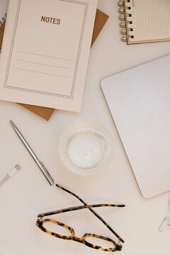 Vertical Flat Lay Of Modern Desk Setup With Notes Notebook, Closed Laptop, Tortoiseshell Glasses, And Water Glass