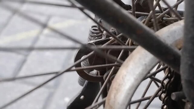 Close-up video of vintage roadster bike drive chain and rear cog turning on rusty metal wheel frame.
