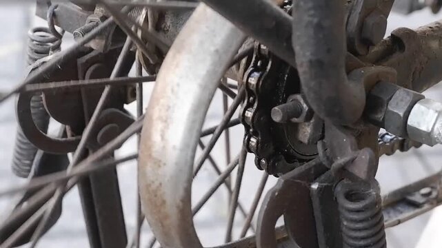 Close-up video of vintage roadster bike drive chain and rear cog turning on rusty metal wheel frame.