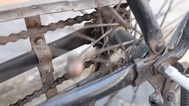 Close-up video of vintage roadster bike drive chain and rear cog turning on rusty metal wheel frame.