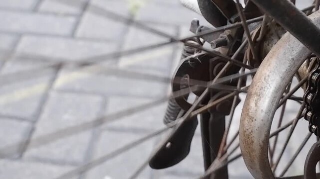 Close-up video of vintage roadster bike drive chain and rear cog turning on rusty metal wheel frame.