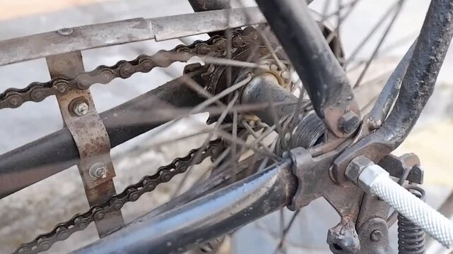 Close-up video of vintage roadster bike drive chain and rear cog turning on rusty metal wheel frame.