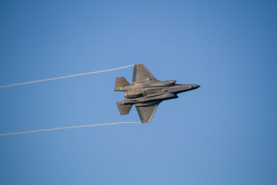 F-35A Lightning II fighter aircraft flying across a blue sky, photographed in side profile showing its distinctive stealth aircraft design.