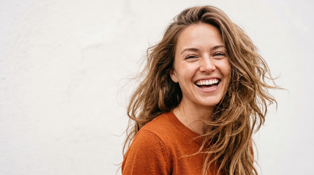 Young woman confidently smiling and laughing, expressing genuine happiness and positivity with wind blowing her long curly hair, portraying a vibrant and authentic lifestyle