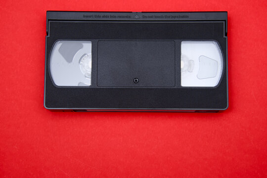 Black analog VHS video cassette on a vibrant red background, representing vintage media and old entertainment technology with copy space