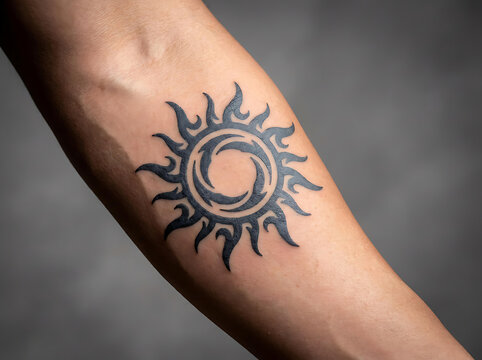 Black tribal sun tattoo inked on a human forearm close up view