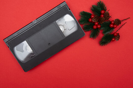 Retro VHS video cassette with festive pine branches and red berries on a vibrant red background, capturing holiday nostalgia with copy space