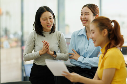 Asian businesswomen collaborating and discussing project ideas in an informal office setting, finding solutions and enjoying a positive team meeting
