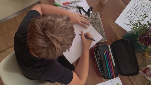 Top-down view of a schoolboy concentrating while completing technical design drawing homework, showing focused study and educational activity.
