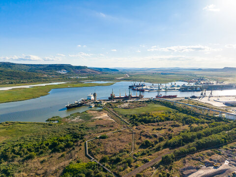 Cargo ships and boats docked at a busy port surrounded by green land and water