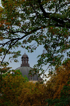 The architectural detail of a classic religious building cupola emerges through the dense canopy of seasonal trees during a crisp fall afternoon