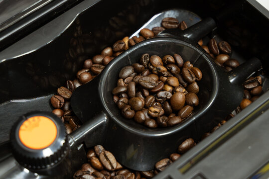 Roasted coffee beans filling the hopper and measuring scoop of an automatic espresso machine