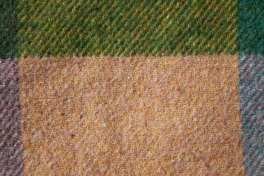 Close-up of authentic vintage wool cashmere with geometric color-block pattern in green, blue, yellow and muted pink. Soft textured woven fabric with natural fibers and rich color transitions.