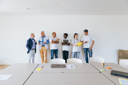 Medical team talking against white wall in empty hospital meeting room